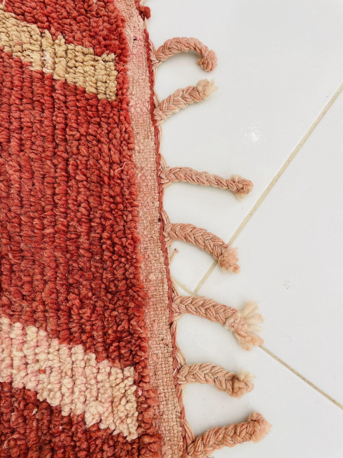 Detail view of a vintage Moroccan rug with a striped design and fringe edges in red and cream.