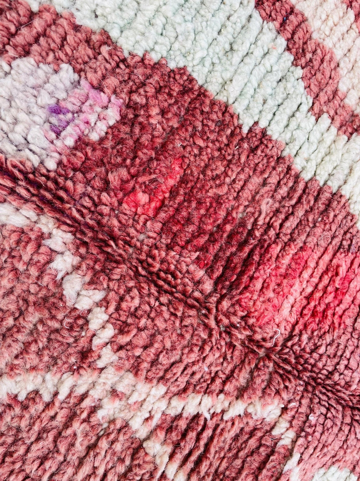 Detail shot of a vintage Moroccan rug displaying tribal patterns and a soft texture in red, pink, and white.