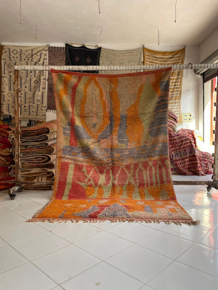 Lifestyle shot of a colorful Moroccan rug featuring orange, blue, and red tones.