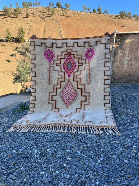 Lifestyle shot of a cream and pink Moroccan rug featuring geometric patterns and fringe edges.