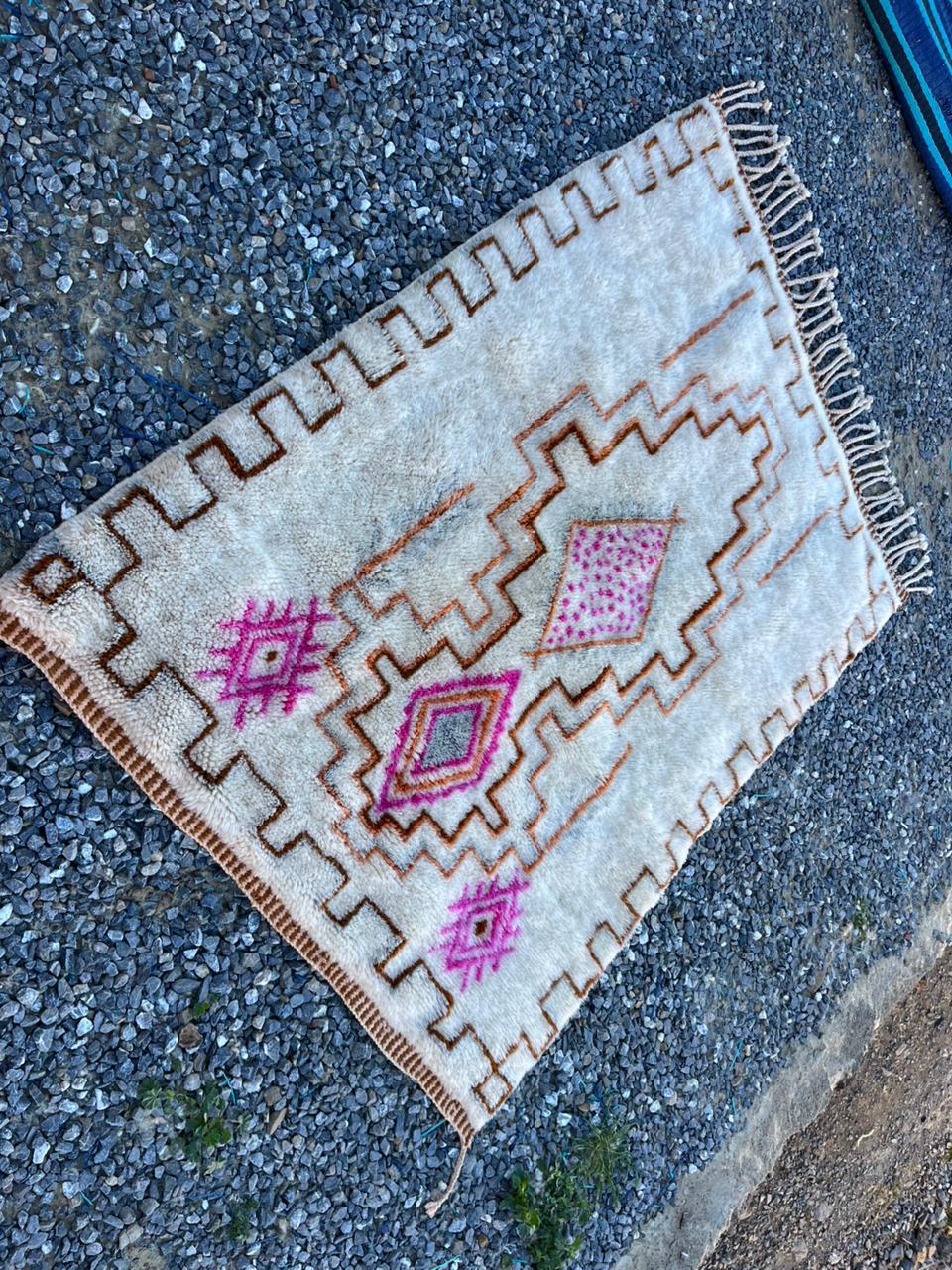 Close-up detail of a cream and pink Moroccan rug highlighting its geometric patterns and fringe edges.