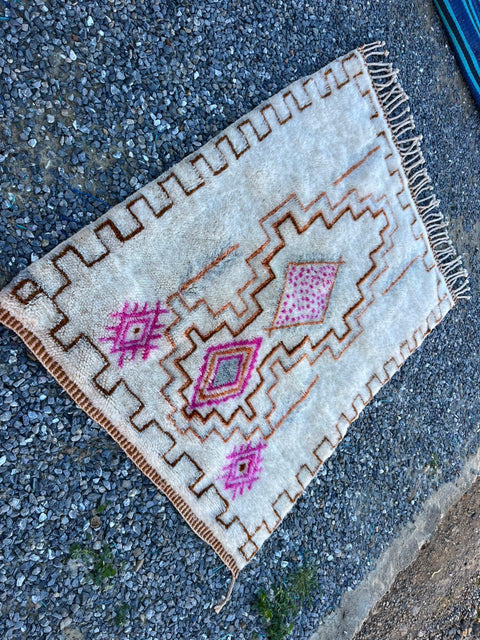 Close-up detail of a cream and pink Moroccan rug highlighting its geometric patterns and fringe edges.
