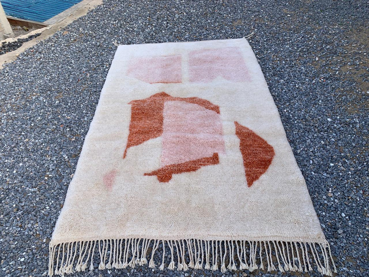Detail close-up of the abstract design and fringe edges of a cream and pink Moroccan rug.