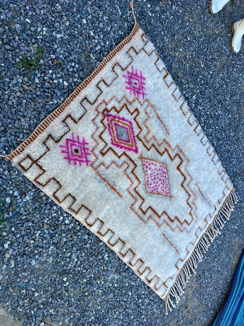 Detailed view of a cream and pink Moroccan rug with geometric patterns and fringe edges.