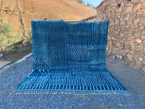 Lifestyle shot of a blue and white abstract Moroccan rug with fringed edges.