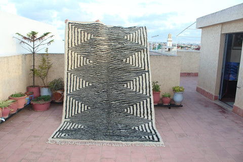 Lifestyle shot of a black and white geometric rug with fringe edges in a natural setting.