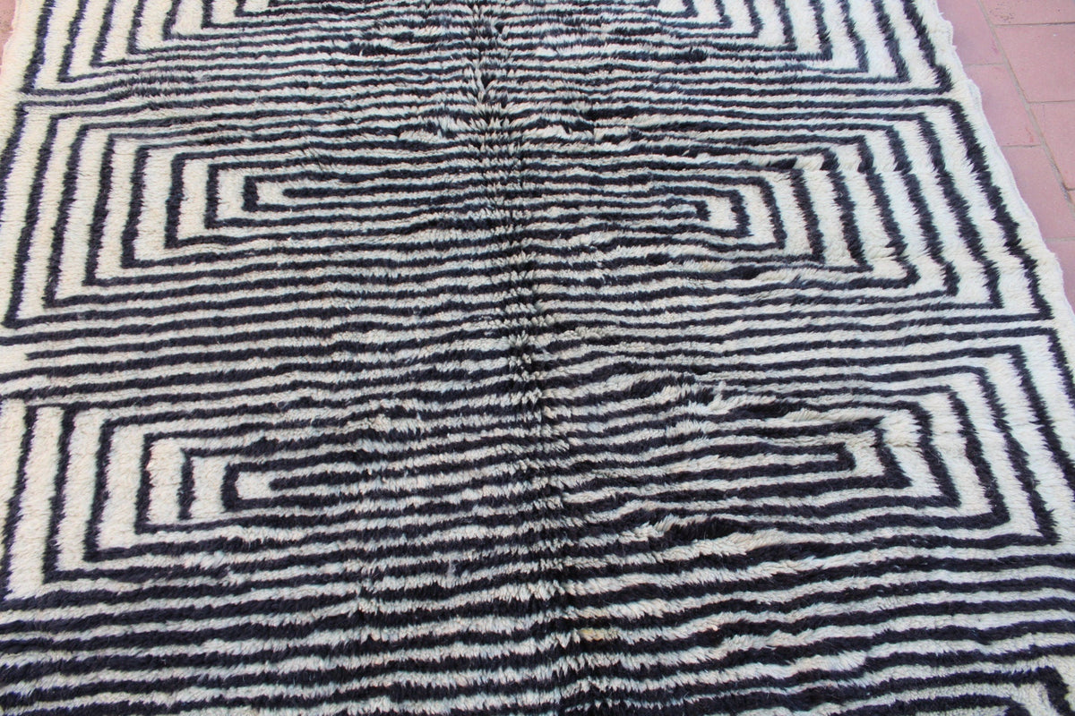 Lifestyle image of a black and white rug with geometric design and fringe edges in a natural background.