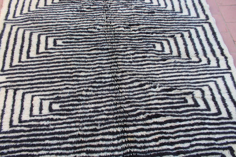 Lifestyle image of a black and white rug with geometric design and fringe edges in a natural background.