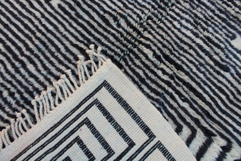 Close-up detail of a black and white rug featuring a striped pattern and fringe edges.