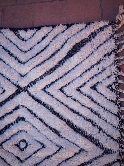 Close-up detail of a diamond pattern and fringe edges on a black and white rug.