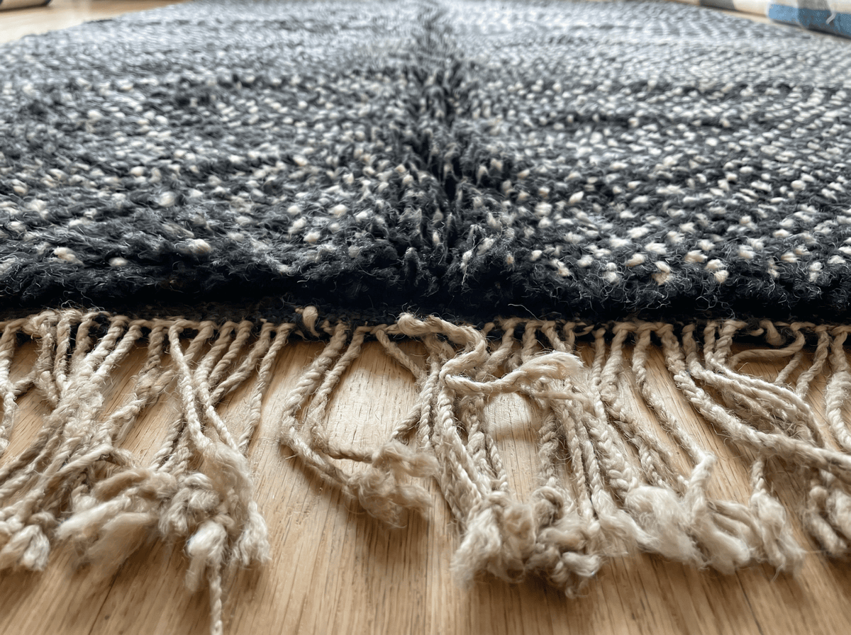 Close-up of a black handmade Moroccan rug displaying a textured pattern and fringe edges.