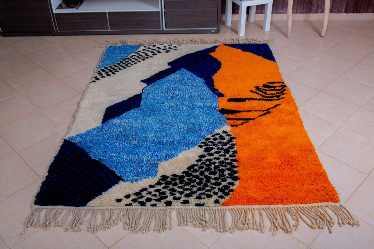 Detail close-up of the corner of a blue Moroccan rug with fringe edges and a textured pattern.