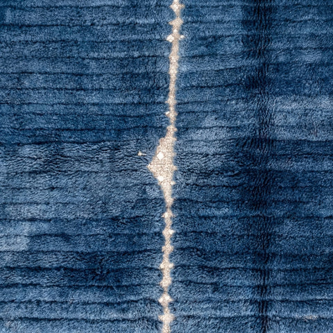 Close-up detail of a blue Moroccan rug highlighting fringe detail against a studio backdrop.