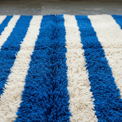 Front view of a blue striped Moroccan rug featuring wide stripes in a studio background.