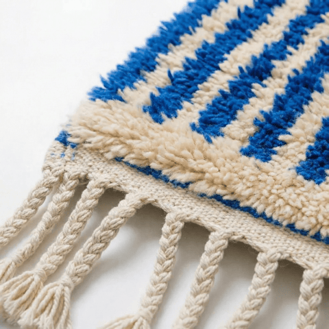 Close-up detail of the textured surface of a blue striped Moroccan rug with fringe edges.