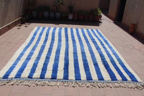 Lifestyle shot of a blue striped rug featuring fringed edges.