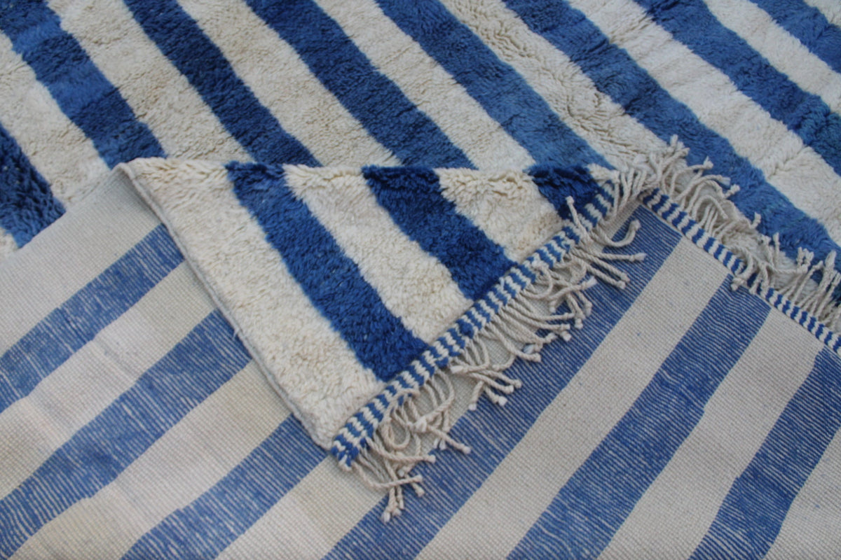 Detail view of a blue striped rug featuring fringe edges.