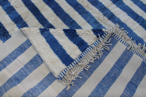 Detail view of a blue striped rug featuring fringe edges.