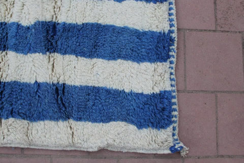 Close-up view of a blue striped rug showing a fringe edge.