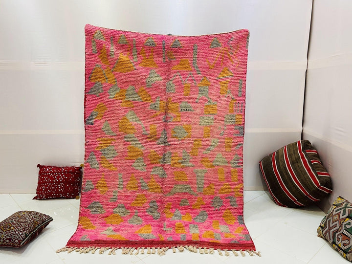 Lifestyle shot of a pink Moroccan rug featuring tribal patterns against a solid background.