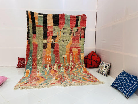 Lifestyle shot of an orange abstract Moroccan rug with green and red accents on a white background.