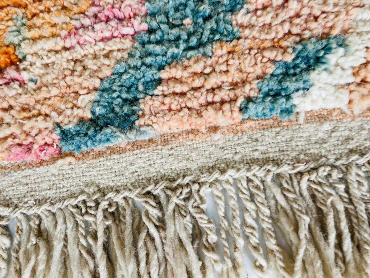 Close-up detail of a beige and orange Moroccan rug with fringe and colorful patterns.