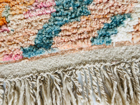 Close-up detail of a beige and orange Moroccan rug with fringe and colorful patterns.