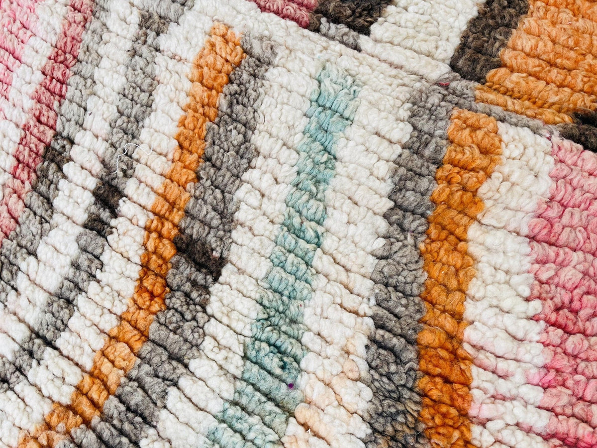 Close-up view of a striped pattern in orange, white, gray, and pink on the rug.