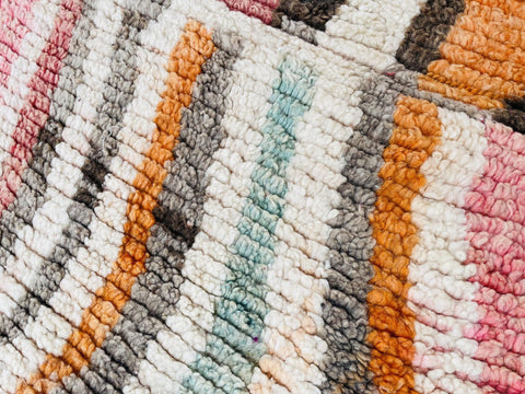 Close-up view of a striped pattern in orange, white, gray, and pink on the rug.