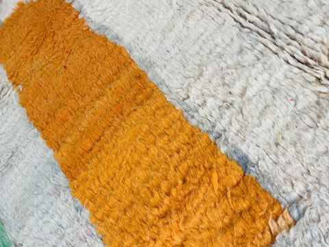 Detail shot of an orange and white textured surface on a pink abstract Moroccan rug.