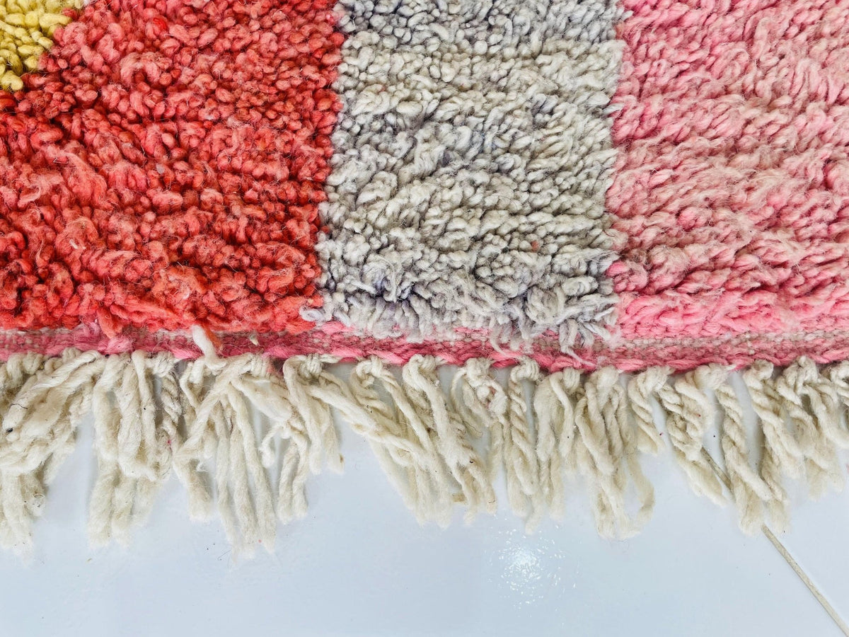 Detail view of the edge of a pink abstract Boujaad Moroccan rug showcasing fringe and color blocks.