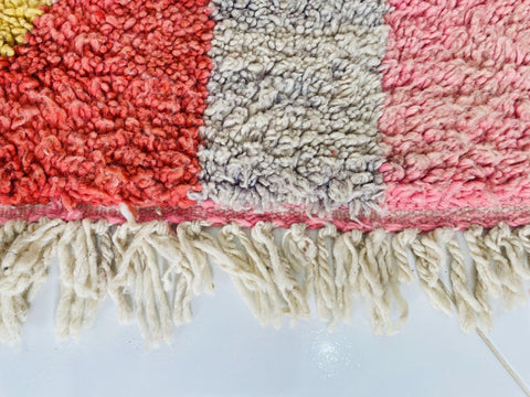 Detail view of the edge of a pink abstract Boujaad Moroccan rug showcasing fringe and color blocks.