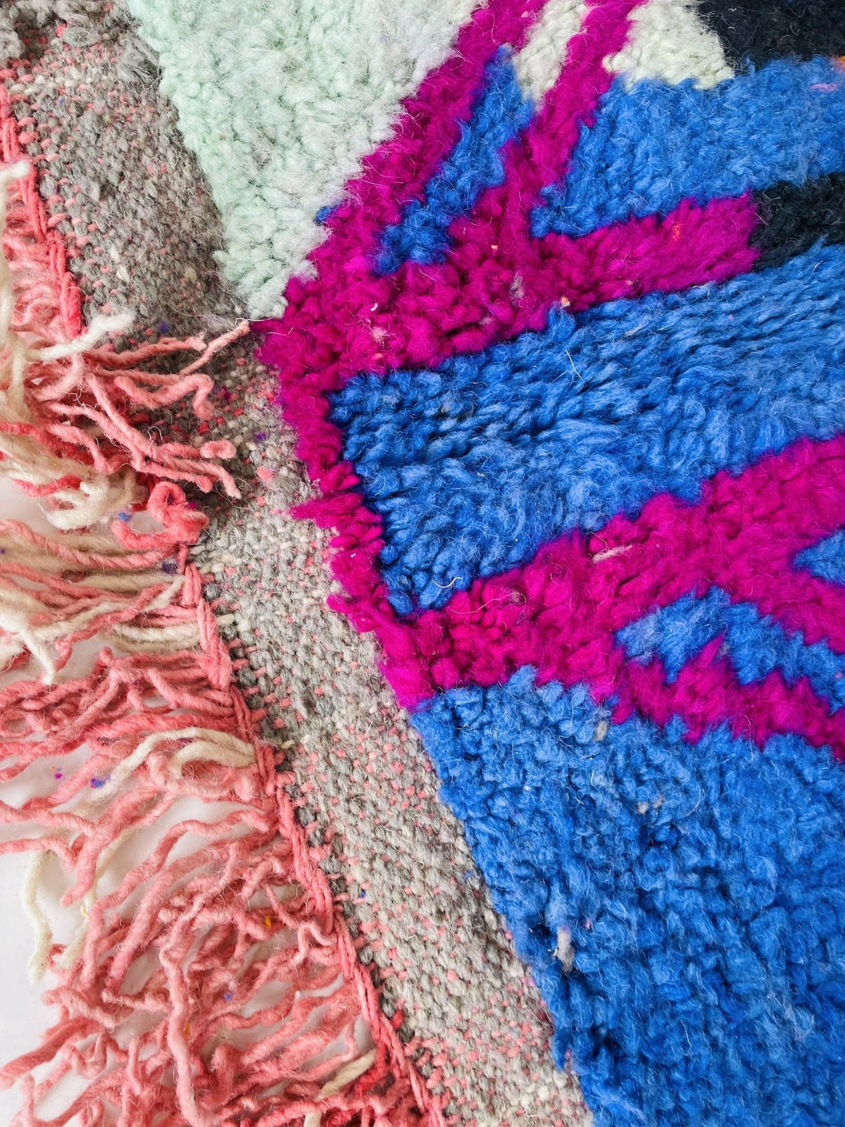 Close-up detail of the textured fibers of a pink and orange abstract Moroccan rug.