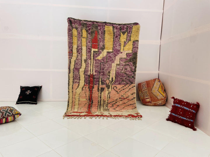 Lifestyle shot of a purple and pink abstract Moroccan rug on a white background.