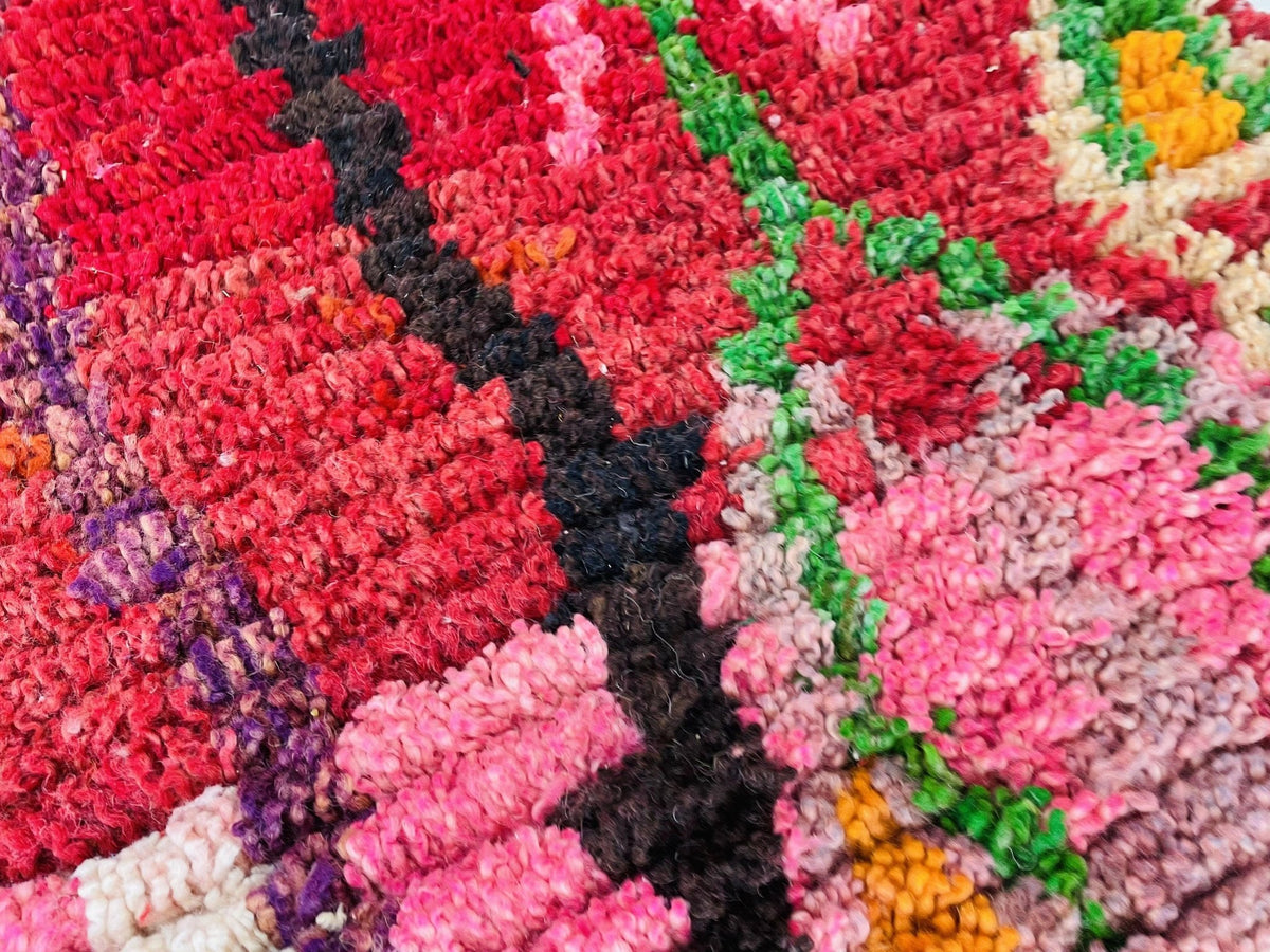 Close-up detail of the rug showing vibrant colors of red, pink, and black in an abstract pattern.