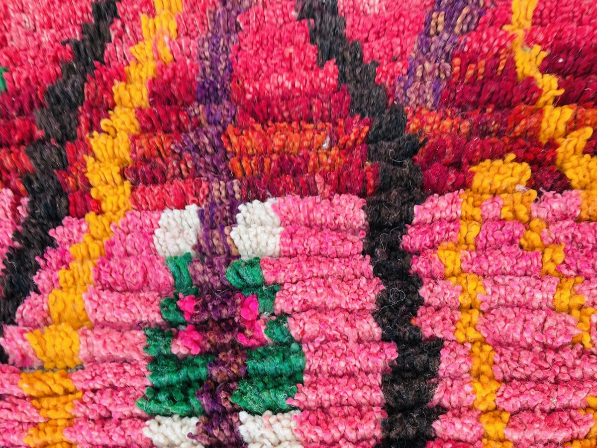Detail shot of the rug displaying handmade abstract design with pink, black, and yellow hues.