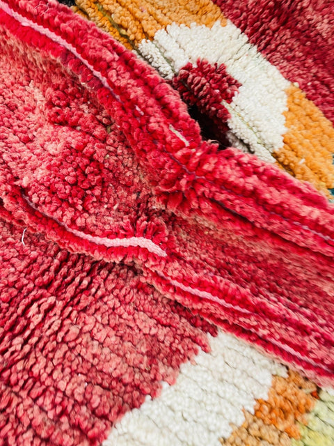 Close-up detail of the textured weave and colorful fibers of a red and pink Moroccan rug.