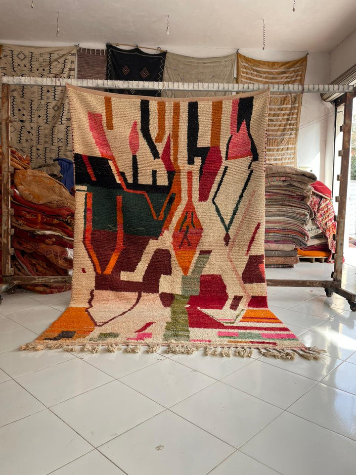 Lifestyle shot of a vintage Moroccan rug featuring geometric patterns in beige, orange, green, and red.