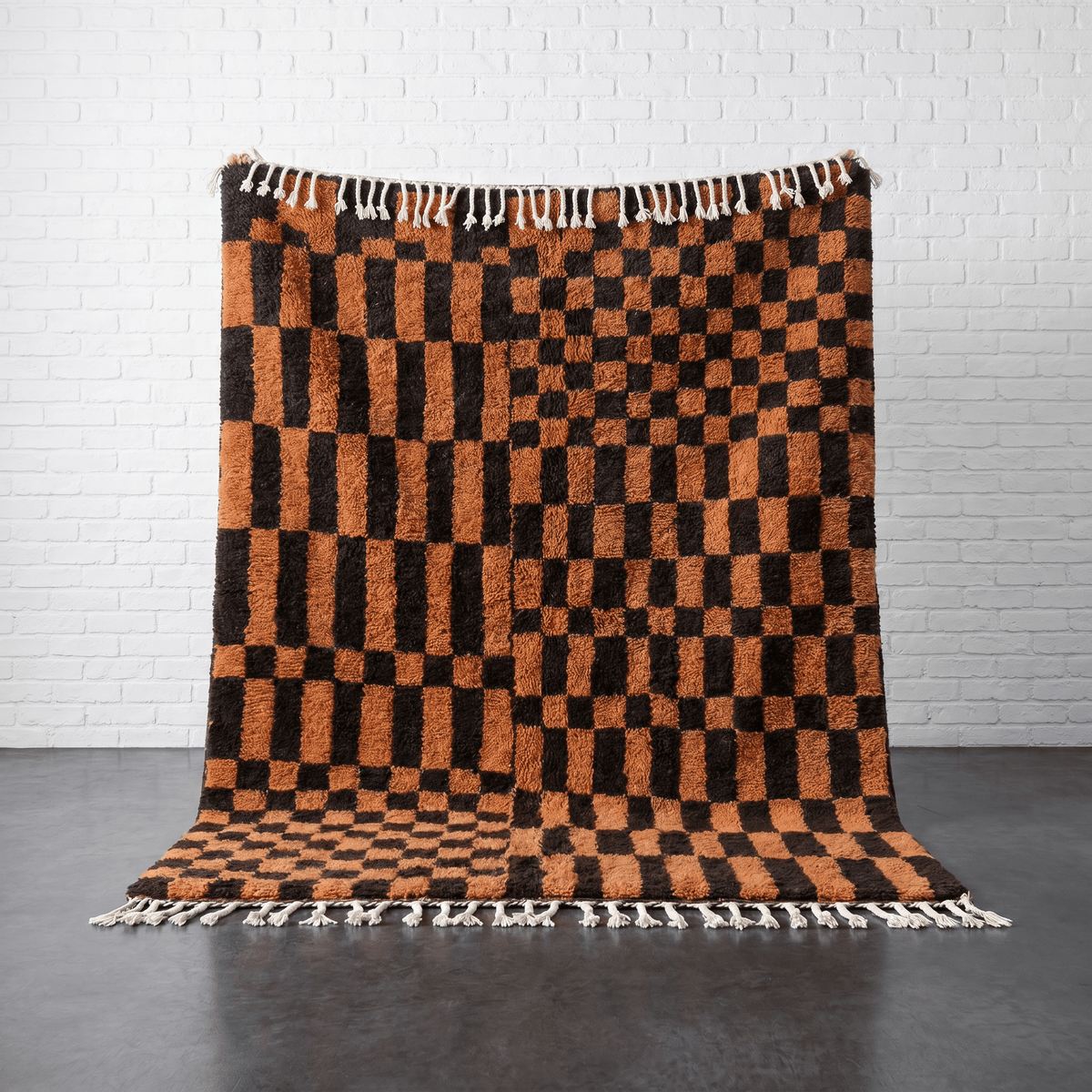Lifestyle shot of a brown checkered rug with fringe edges in a natural setting.