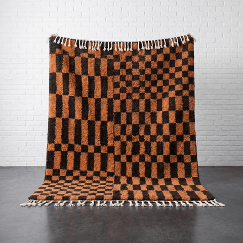 Lifestyle shot of a brown checkered rug with fringe edges in a natural setting.