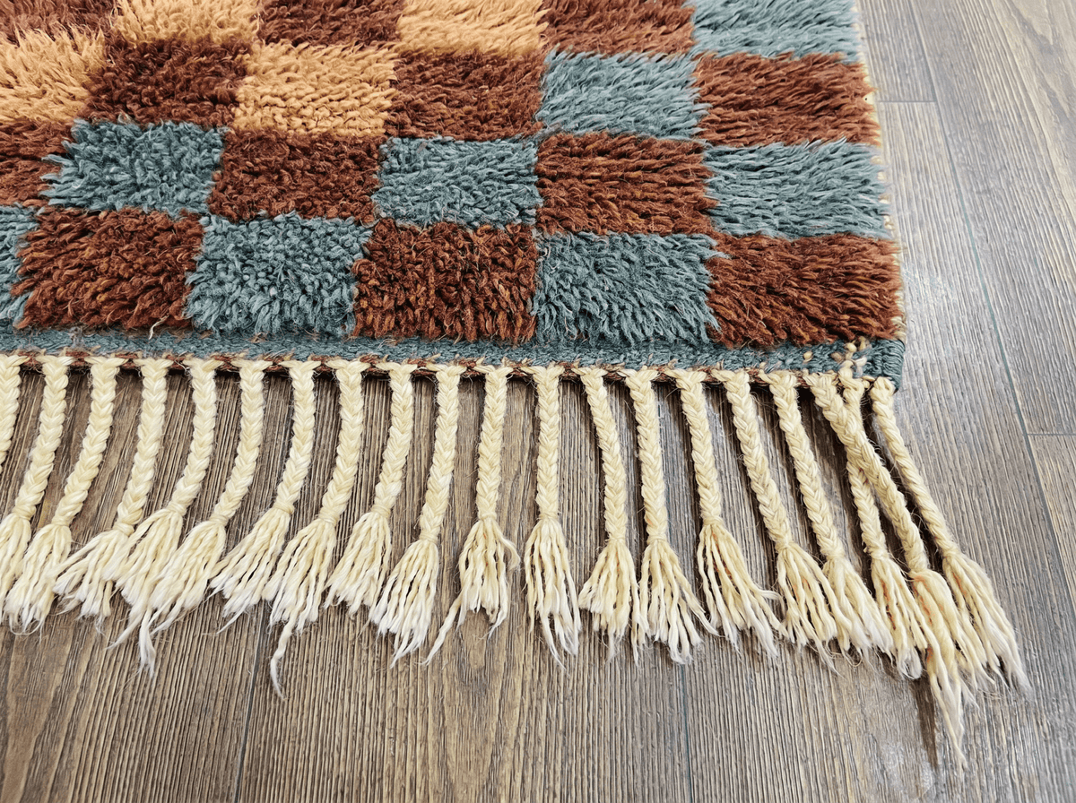 Detail view of a burgundy checkered Moroccan rug featuring fringe details and a natural background.