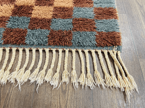 Detail view of a burgundy checkered Moroccan rug featuring fringe details and a natural background.