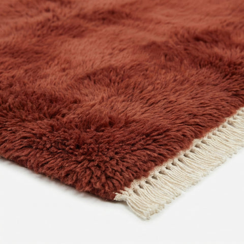 Close-up detail showing the fringe edges and thick pile of the burgundy red Moroccan rug.