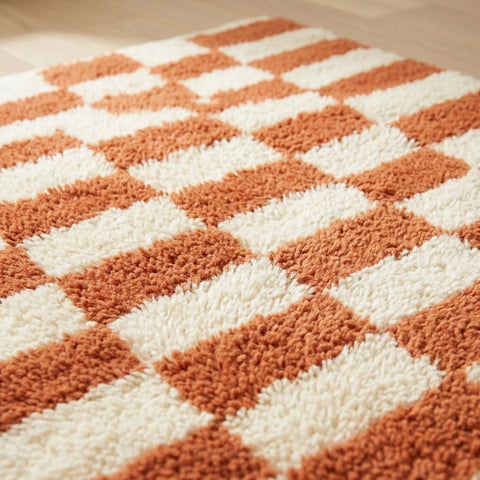 Lifestyle image of a checkered terracotta rug with a soft pile in a natural setting.