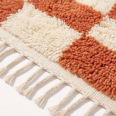 Close-up detail of the checkered terracotta rug showcasing its fringe edges and textured surface.