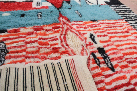 Detail close-up of a Moroccan rug showing varied textures and geometric shapes in red, blue, and black.