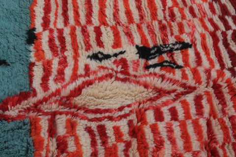 Detail close-up of a Moroccan rug with a striped pattern and abstract design in red, black, and beige.