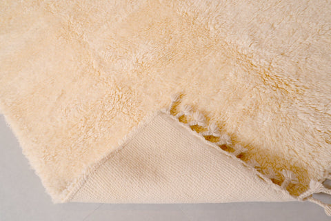 Close-up detail of the off-white Moroccan rug featuring fringe detail and a thick pile.