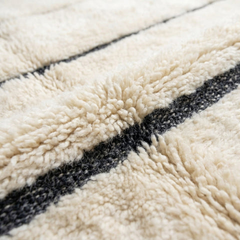 Detail close-up of a cream tufted Moroccan rug with a black stripe on a white background.