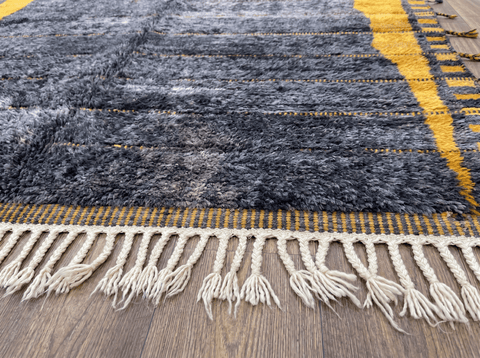 Close-up of the dark grey Moroccan rug with fringe edges and textured surface in a natural setting.